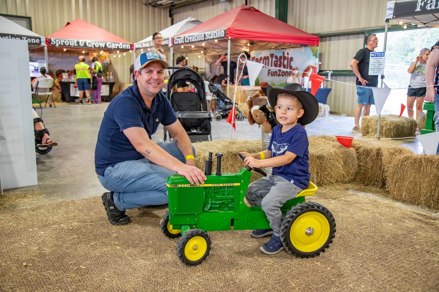 A dad watches his son ride a pedal tractor at the fair